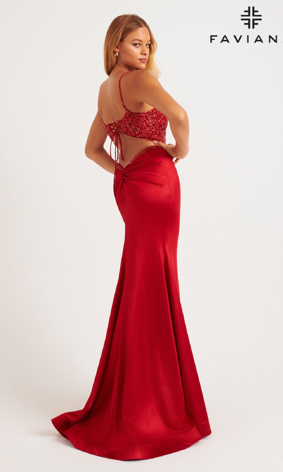 Woman in a red, backless satin Faviana 11256 prom dress with lace-up detail and a subtle leg slit, standing slightly turned away; Faviana logo appears in the top right corner.